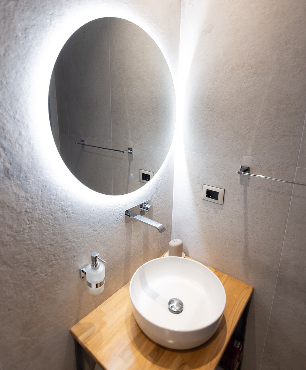 A bathroom with a round mirror, a white sink, and a wooden vanity.