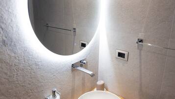 A bathroom with a round mirror, a white sink, and a wooden vanity.
