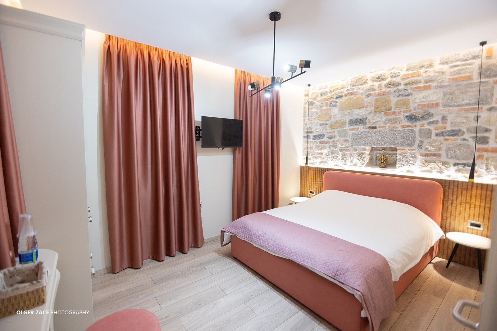 A bedroom with a bed, curtains, a television, a stone wall, and a small table.
