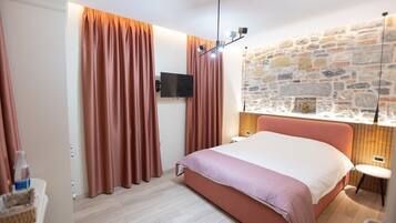 A bedroom with a bed, curtains, a television, a stone wall, and a small table.