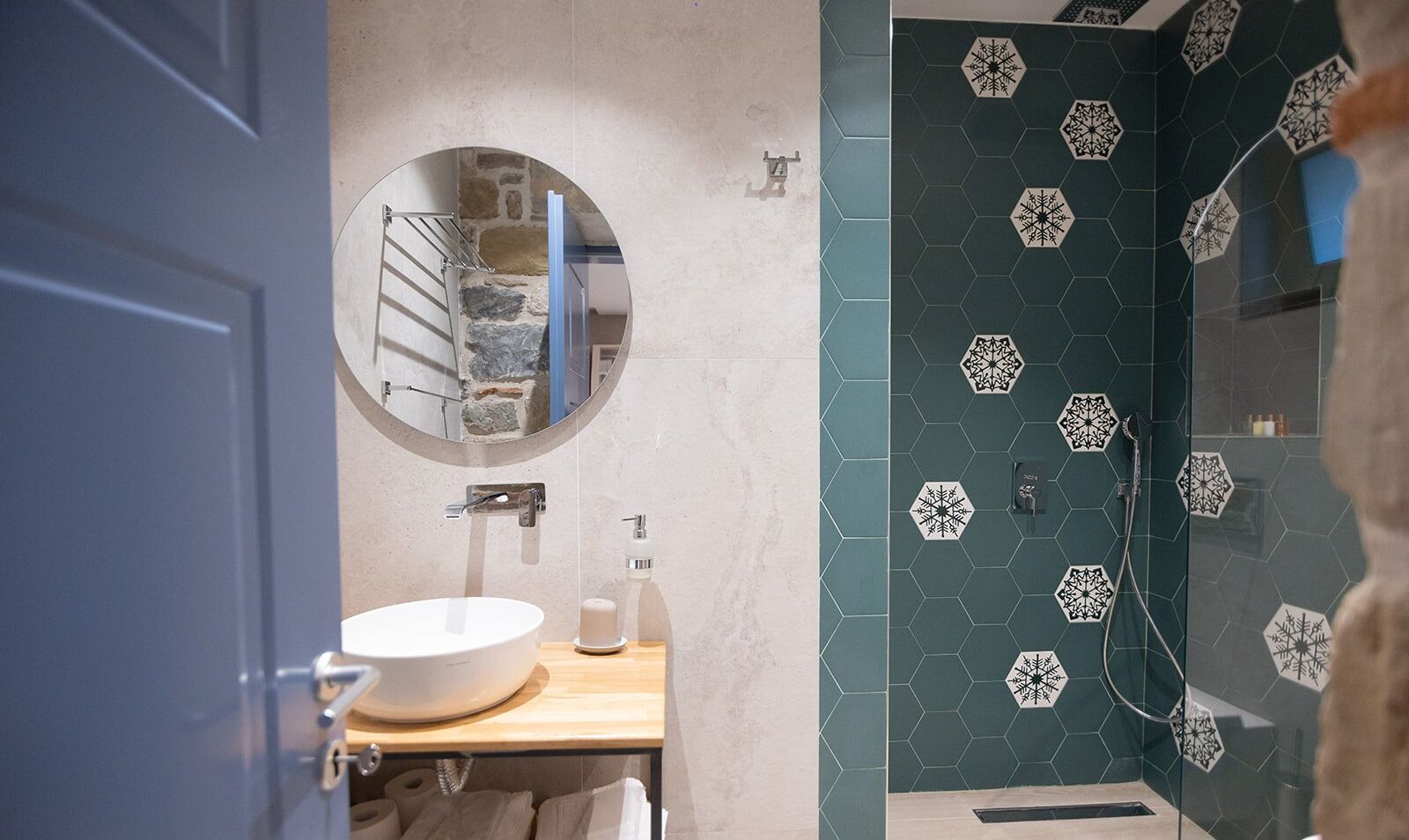 Une salle de bain avec un miroir rond, un lavabo blanc et une douche aux carreaux hexagonaux.