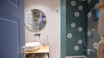 Une salle de bain avec un miroir rond, un lavabo blanc et une douche aux carreaux hexagonaux.