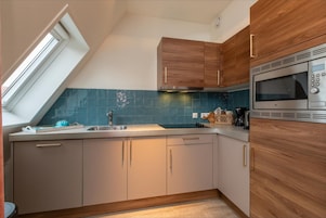 A kitchen with a skylight, wooden cabinets, a stainless steel microwave, and a blue-tiled backsplash.