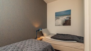 Une chambre avec deux lits, un mur orné d’un motif, un tableau représentant une plage et une table de chevet avec une lampe.