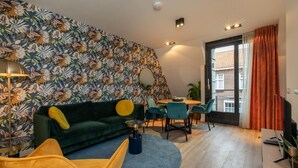 Un salon moderne avec un canapé vert, un fauteuil jaune et un coin repas comprenant une table et des chaises.