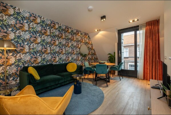 A modern living room with a green sofa, yellow armchair, and a dining area with a table and chairs. - Apartment in Zoutelande Near the Beach (Zoutelande)