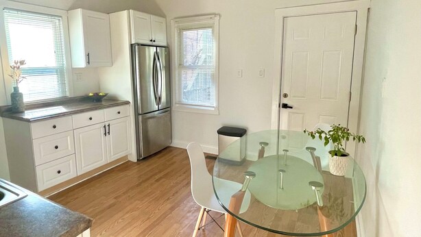 A modern kitchen with white cabinets, a stainless steel refrigerator, a glass dining table, and a black and white striped ceiling light.