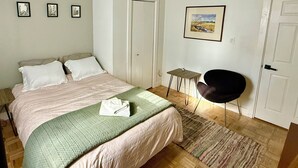 A bedroom with a bed, a chair, a small table, and a door.