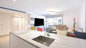 A modern kitchen with a marble countertop and sink, a dining area with colorful chairs, and a living room with a sofa and decorative pillows. - 3BR Beach&City Vibes in Bugrashov by HolyGuest (Tel Aviv-Yafo)