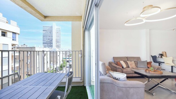 A balcony with a table and chairs, a sofa, and a coffee table. - 3BR Beach&City Vibes in Bugrashov by HolyGuest (Tel Aviv-Yafo)