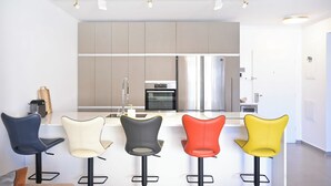 A modern kitchen with five bar stools, a stainless steel refrigerator, and a built-in oven. - 3BR Beach&City Vibes in Bugrashov by HolyGuest (Tel Aviv-Yafo)