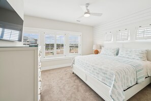 A bedroom with a bed, a nightstand, a lamp, a ceiling fan, and a window with blinds. - Daniels -- Brand New Luxury Oceanfront Home (Corolla)