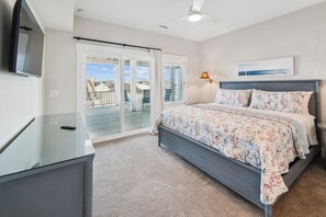 A bedroom with a bed, a desk, a chair, a TV, a ceiling fan, and a view of the beach through the glass door. - Daniels -- Brand New Luxury Oceanfront Home (Corolla)