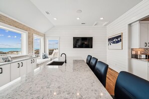 A modern kitchen with a marble countertop, a built-in sink, and a dining area with black leather chairs. - Daniels -- Brand New Luxury Oceanfront Home (Corolla)