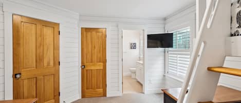 Un couloir avec des portes en bois, un escalier et une vue sur une salle de bain.