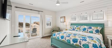 A bedroom with a bed, a desk, a chair, a TV, and a view of the outdoors.