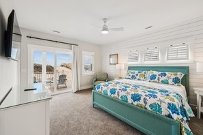 A bedroom with a bed, a desk, a chair, a TV, and a view of the outdoors.