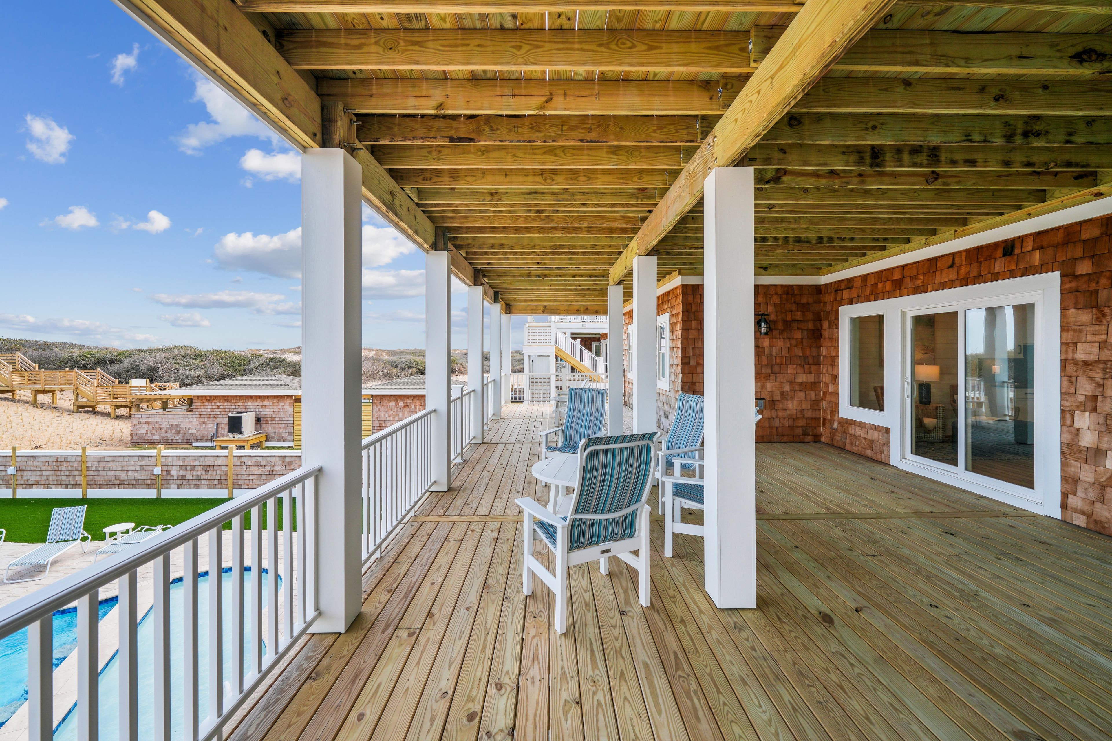 A wooden deck with a pool, outdoor seating, and a view of the beach.