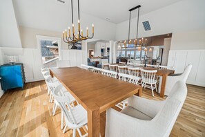 A modern kitchen with a central island, white cabinetry, and a view to the outside. - Daniels -- Brand New Luxury Oceanfront Home (Corolla)