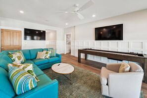 Un salon moderne avec un canapé de couleur turquoise, une table basse ronde, une table de billard et un ventilateur de plafond.