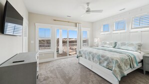 A bedroom with a bed, a desk, a ceiling fan, and a view of the outdoors through the windows. - Owens -- Brand New 12 BR Luxury Oceanfront (Corolla)