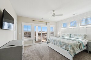 Ein Schlafzimmer mit Bett, Schreibtisch, Deckenventilator und Blick ins Freie durch die Fenster.