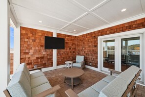 Un espace extérieur aménagé, abrité, avec un téléviseur à écran plat fixé au mur, des sièges rembourrés et une porte vitrée donnant sur l’extérieur.