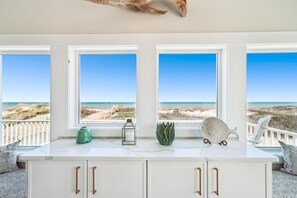 Een kamer met een witte kast, drie ramen met uitzicht op het strand en decoratieve objecten op de vensterbank.
