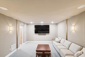 Un salon doté d’un téléviseur à écran plat fixé au mur, d’une table basse en bois, d’un canapé beige et de deux appliques murales.