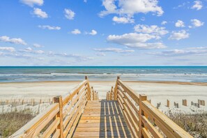 Une promenade en bois menant à une plage, avec un ciel dégagé.