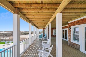 Une terrasse en bois avec des chaises blanches et une piscine, donnant sur une plage.