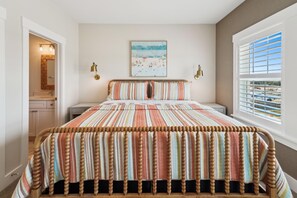 Een slaapkamer met een groot bed, een raam met luxaflex, een nachtkastje, een wandlamp en een lijst met een afbeelding aan de muur.