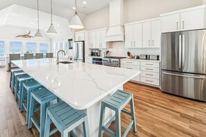 Een moderne keuken met een groot eiland, roestvrijstalen apparatuur en uitzicht op de oceaan.
