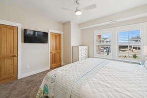 Une chambre à coucher avec un lit, une télévision, un ventilateur de plafond et une fenêtre donnant sur des immeubles.