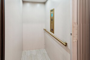 Un ascenseur étroit et vide, doté d’une main courante métallique et d’un panneau de commande fixé au mur.