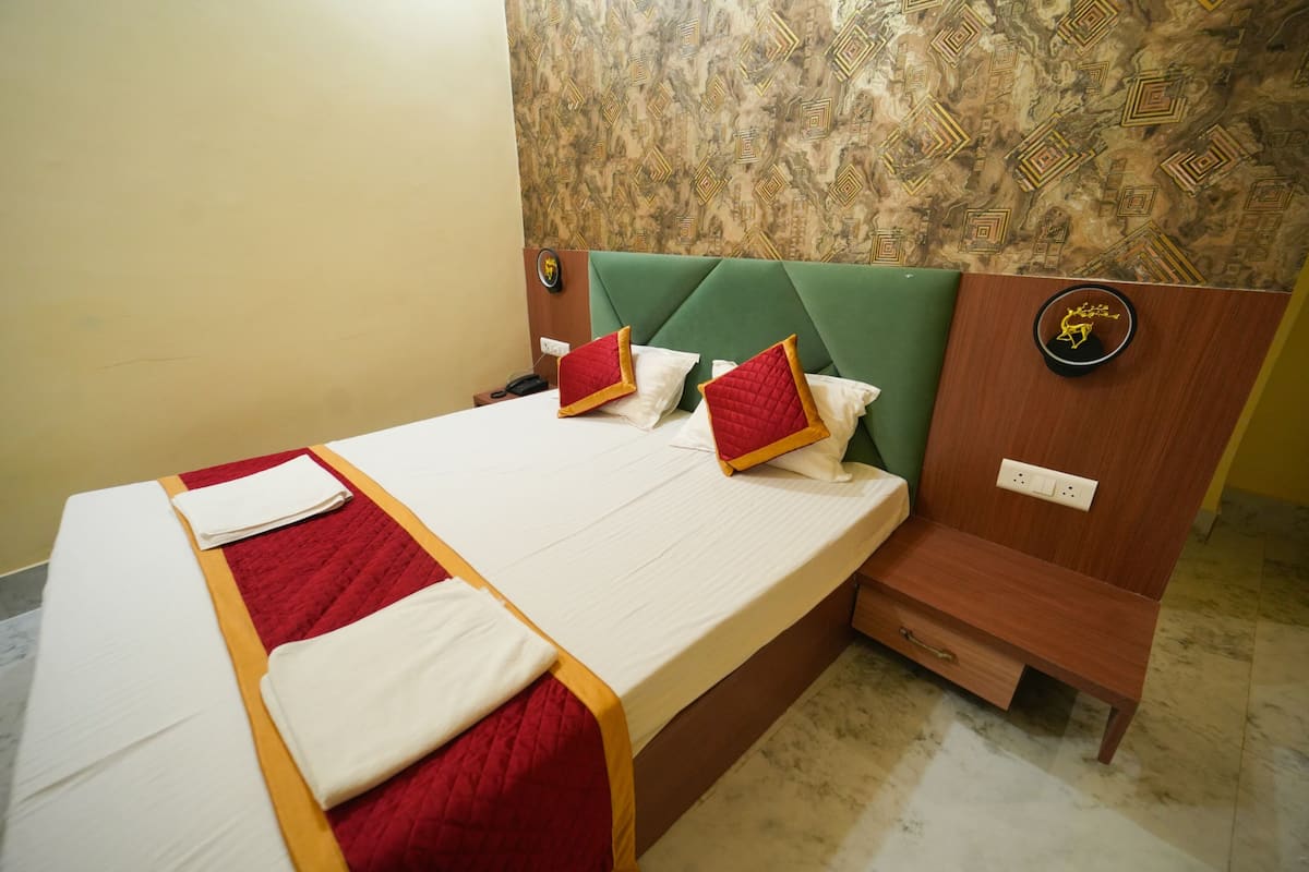 A neatly made bed with red and white bedding, a green upholstered headboard, and a wooden nightstand with a power outlet.