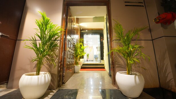 A hotel entrance with a polished floor, two large potted plants, and a red fire extinguisher on the wall. - Kashi Pilgrim Stay (Varanasi)