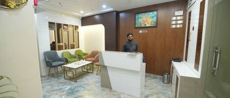 A reception area with a marble floor, wooden paneling, a reception desk, and seating with a green and blue chair.