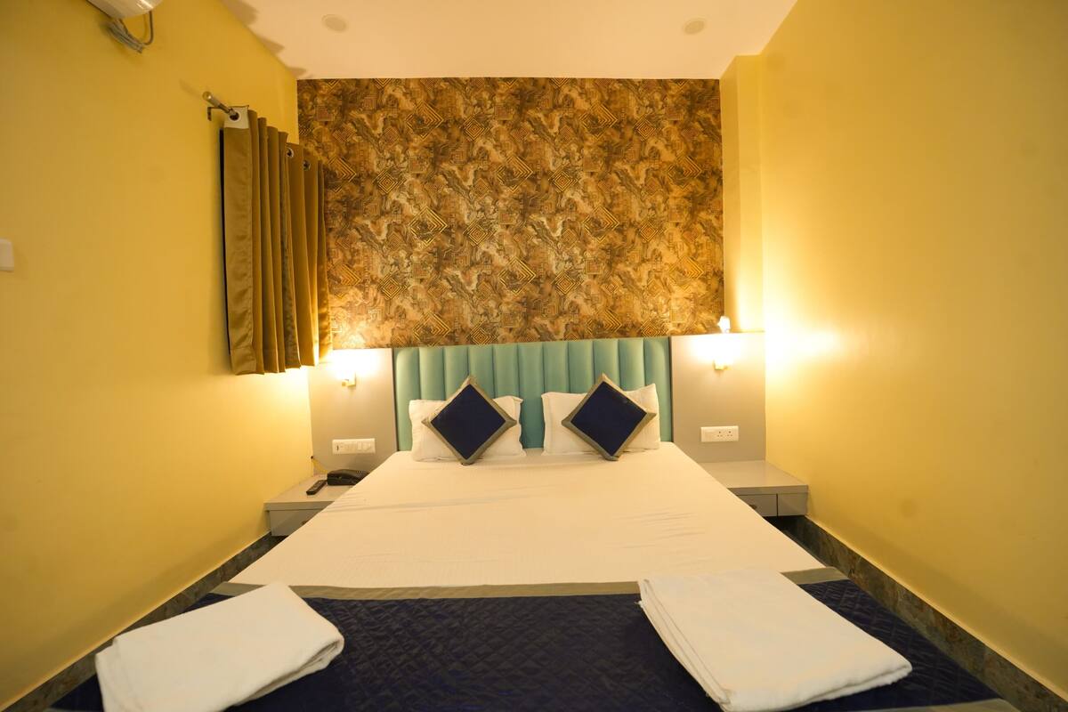A hotel room with a large bed, two bedside tables, a headboard with a patterned design, and a curtain on the left side.