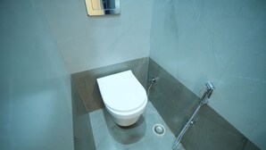A bathroom with a white toilet, a shower, and a drain. - Kashi Pilgrim Stay (Varanasi)