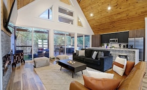 A spacious living area with a high ceiling, a modern kitchen, and large sliding glass doors leading to an outdoor deck.