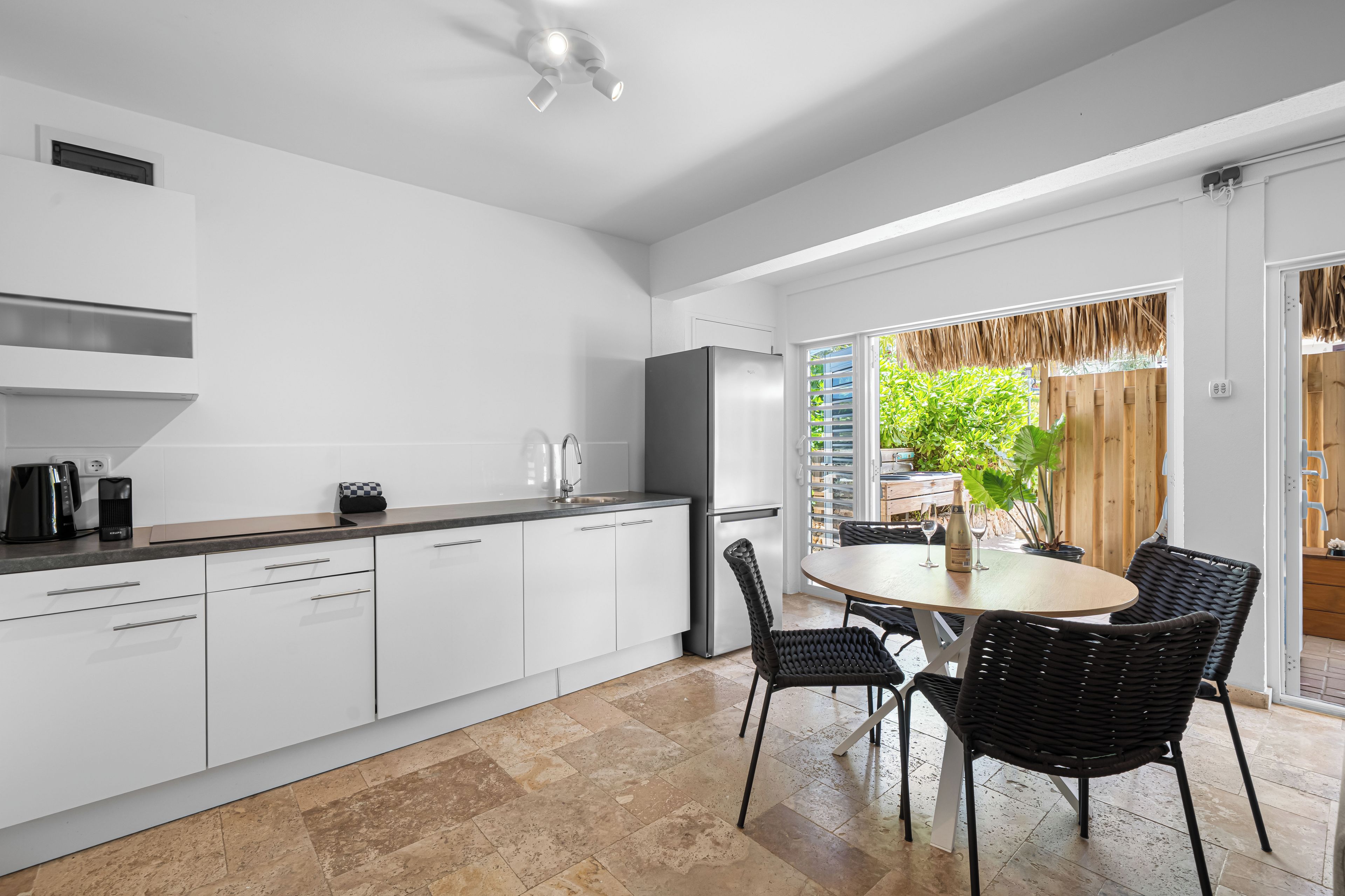 A modern kitchen with white cabinetry, a stainless steel refrigerator, and a dining area with a round table and black chairs.