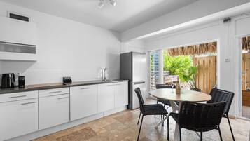 A modern kitchen with white cabinetry, a stainless steel refrigerator, and a dining area with a round table and black chairs.