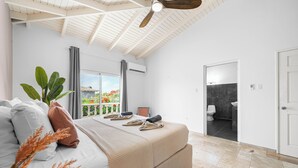 Un dormitorio con cama, ventilador de techo, ventana con cortinas y vistas al exterior.