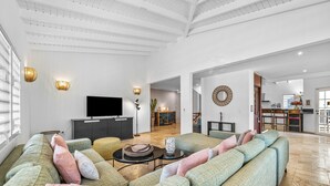 Uma sala de estar espaçosa com um sofá seccional grande, uma televisão de tela plana e um espaço de refeições ao fundo.