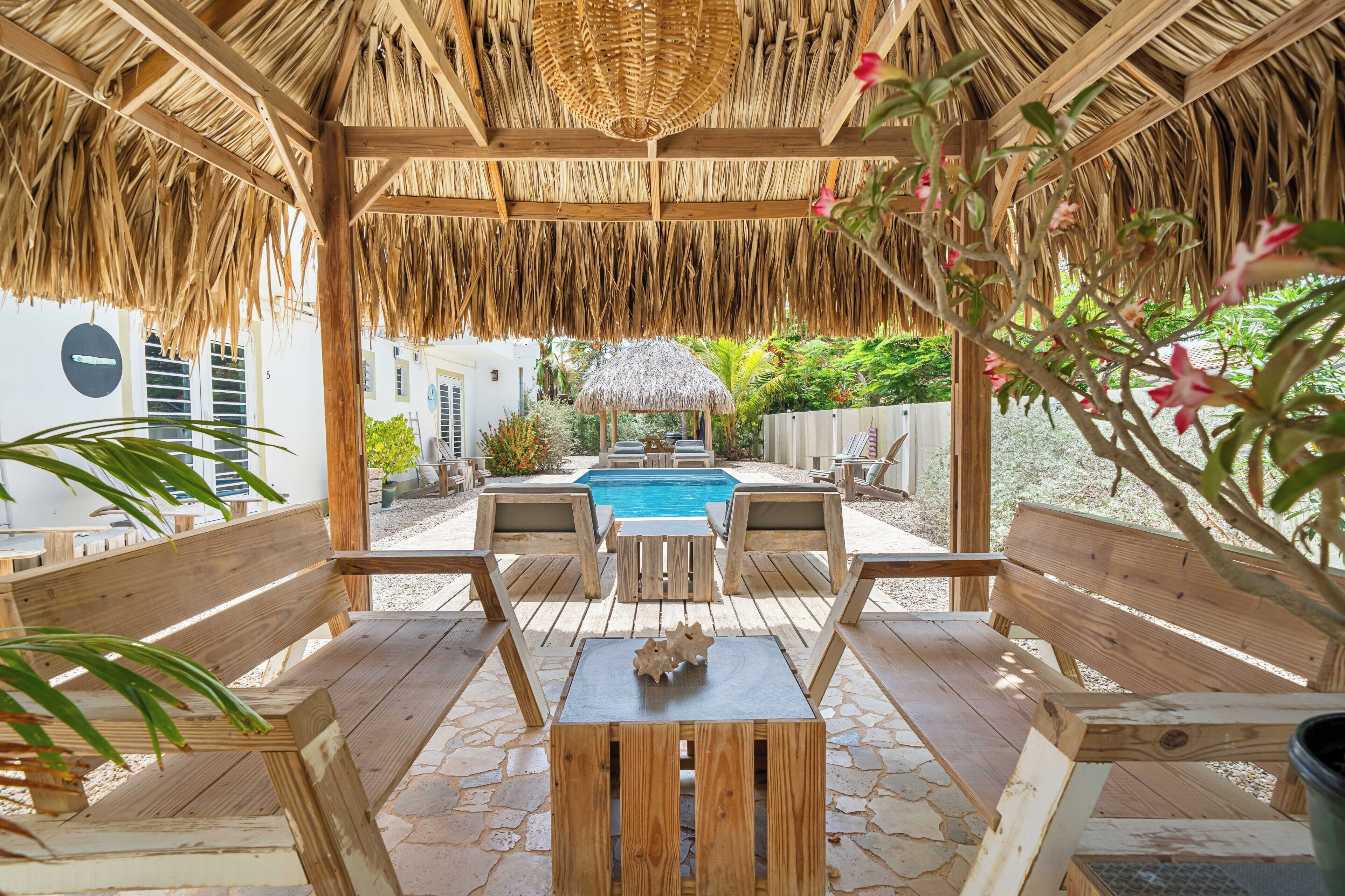 A wooden deck with a thatched roof, a pool, and outdoor furniture.