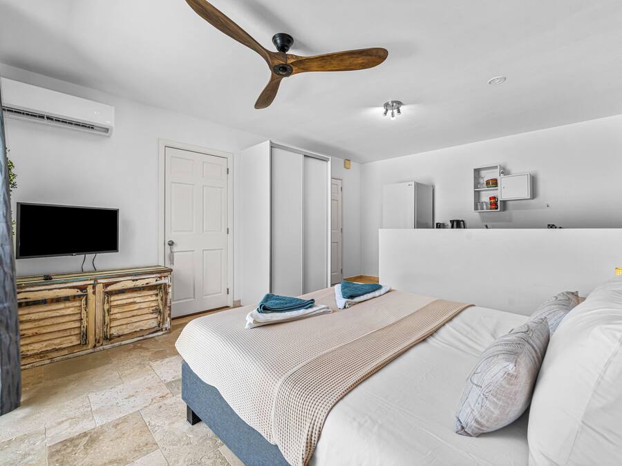 Ein Schlafzimmer mit Bett, Deckenventilator, Fernseher, Kleiderschrank und Spiegel im Badezimmer.