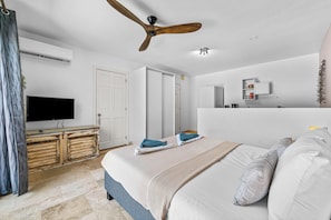 A bedroom with a bed, ceiling fan, TV, wardrobe, and a bathroom mirror. - Bliss Bonaire by Boutique Bonaire Unique Resorts (Kralendijk)