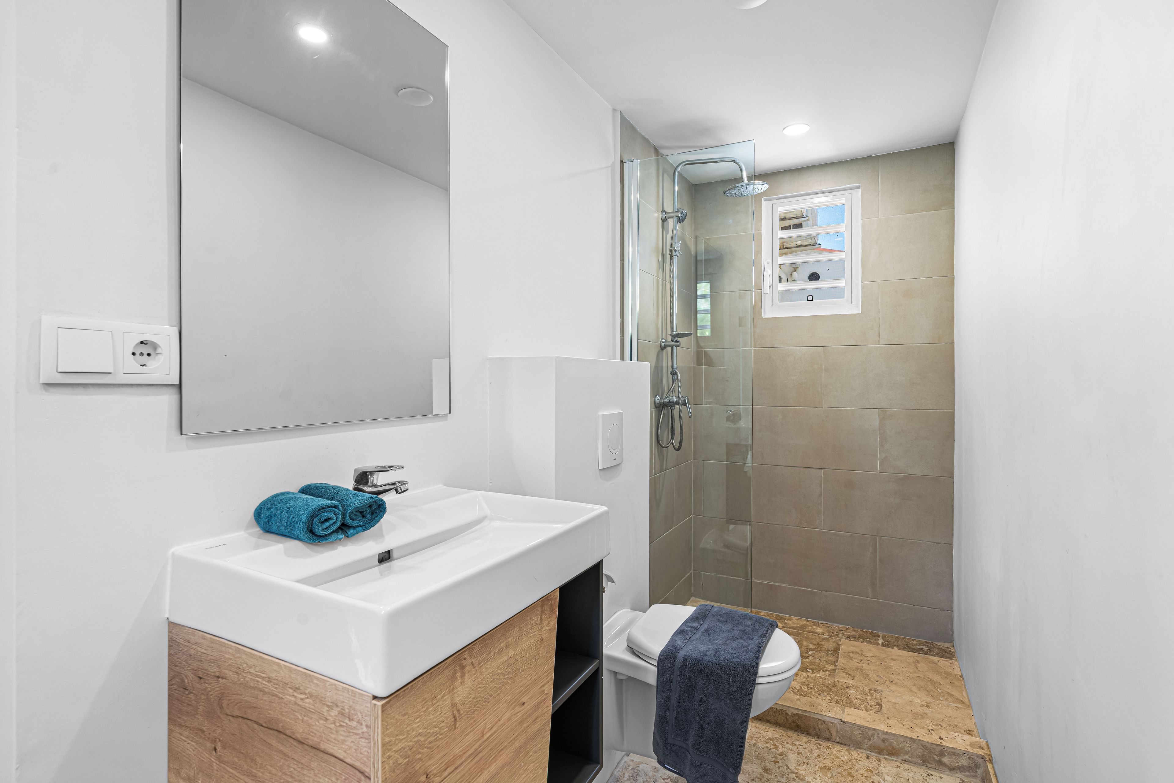 A modern bathroom with a white sink, a mirror, a shower with a glass door, and a toilet.