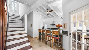 Uma escadaria leva a uma cozinha com um ventilador de teto, uma sala de jantar com cadeiras e uma janela grande.